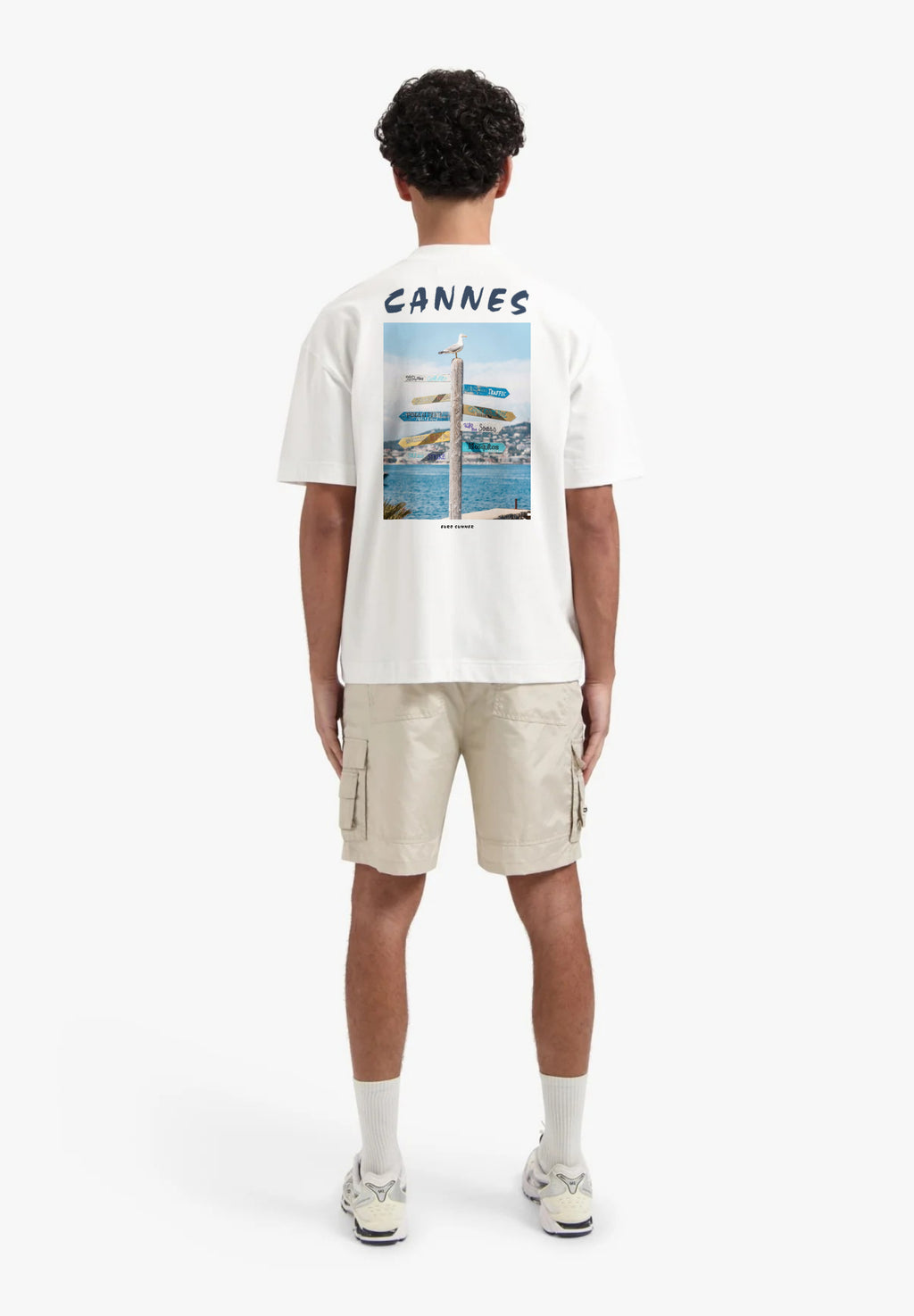 Person wearing a white t-shirt with 'Cannes' print and beige cargo shorts on a white background