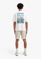 Person wearing a white t-shirt with 'Cannes' print and beige cargo shorts on a white background