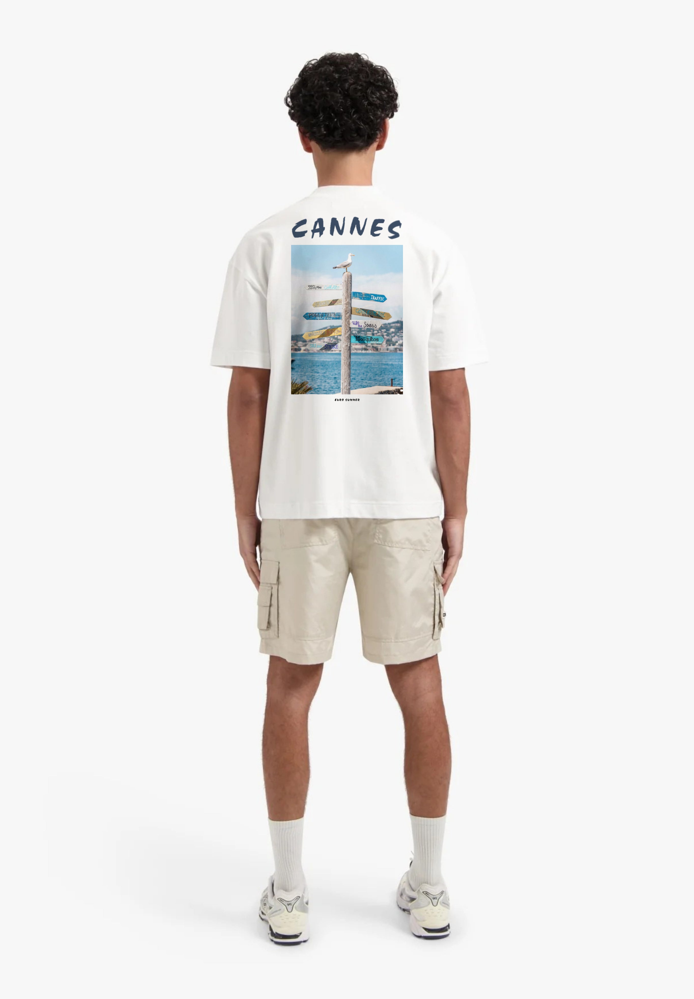 Person wearing a white t-shirt with 'Cannes' print and beige cargo shorts on a white background