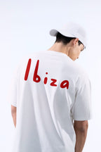 Person wearing a white t-shirt with 'Ibiza' printed on the back, standing against a light background.