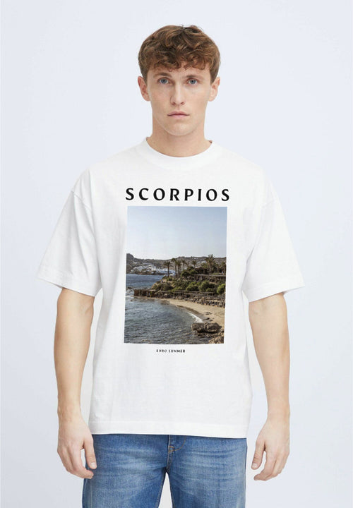 Person wearing a white t-shirt with 'Ibiza' on the back, standing by a pool with mountains in the background.