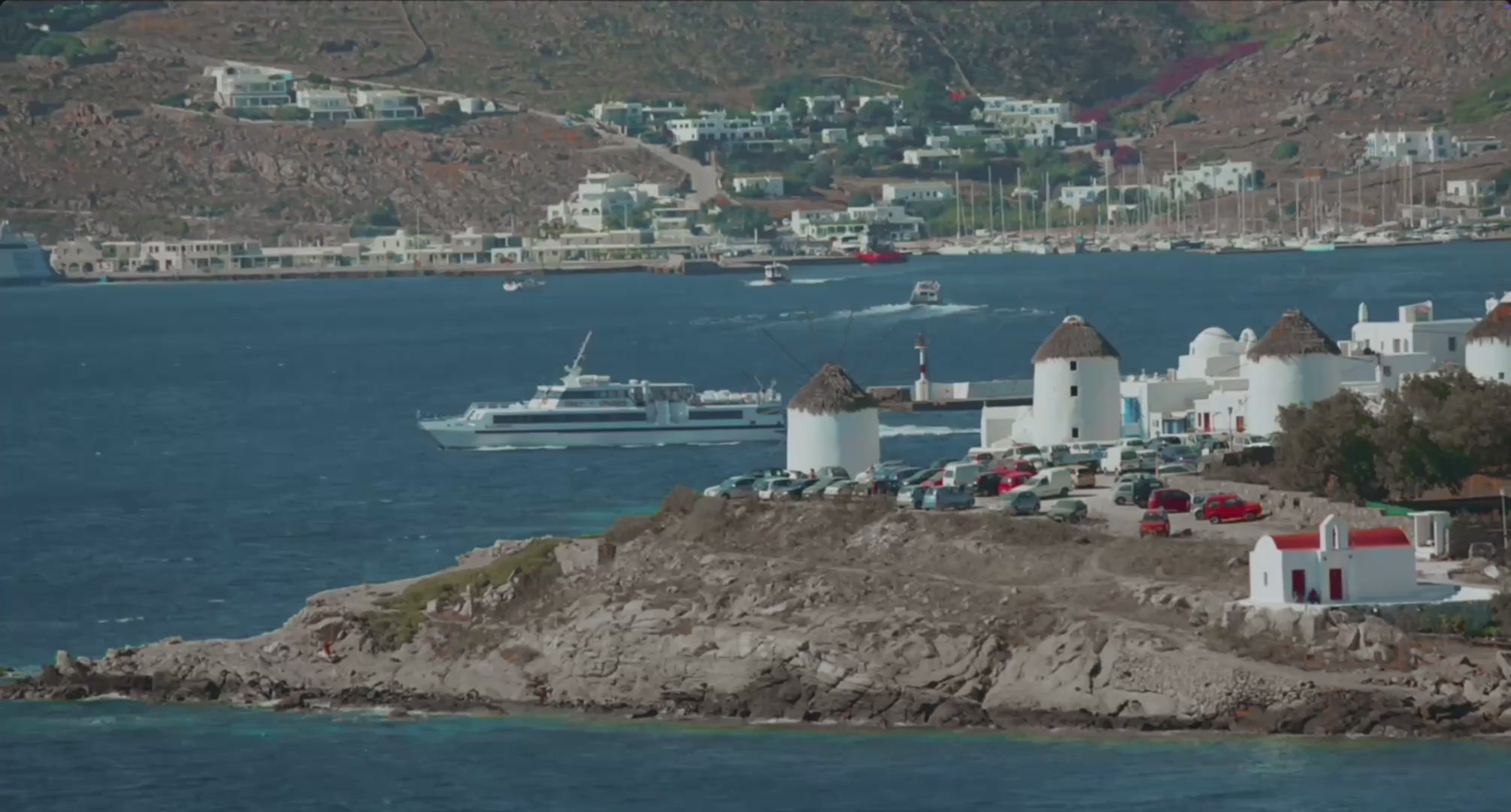 Mykonos coastline view with a yacht passing by and some mediterranean houses
